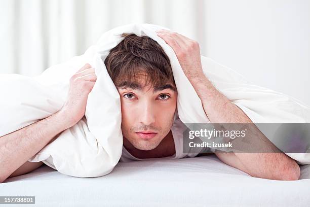 junger mann liegt auf dem bauch unter einer weißen decke - day after party stock-fotos und bilder
