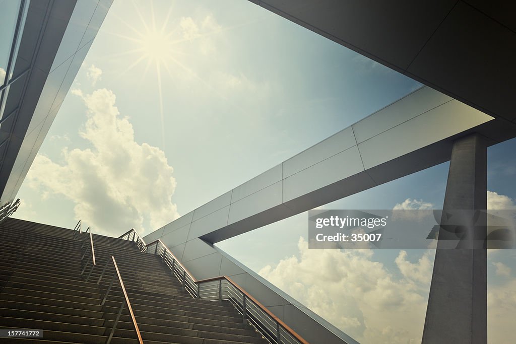 A stairway leading up to blue sky with sun over light cloud