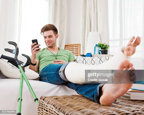 young man with broken leg at home - man crutches stock pictures, royalty-free photos & images