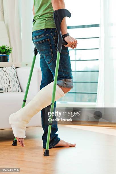 hombre con pierna fracturada en su casa - crutches fotografías e imágenes de stock