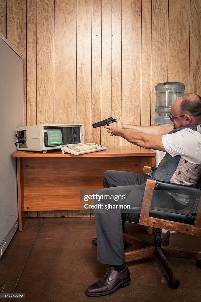 Angry office working aiming gun at old computer