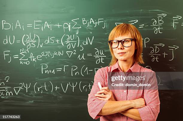 female teacher in horn rimmed glasses is standing against blackboard - natuurkundige stockfoto's en -beelden