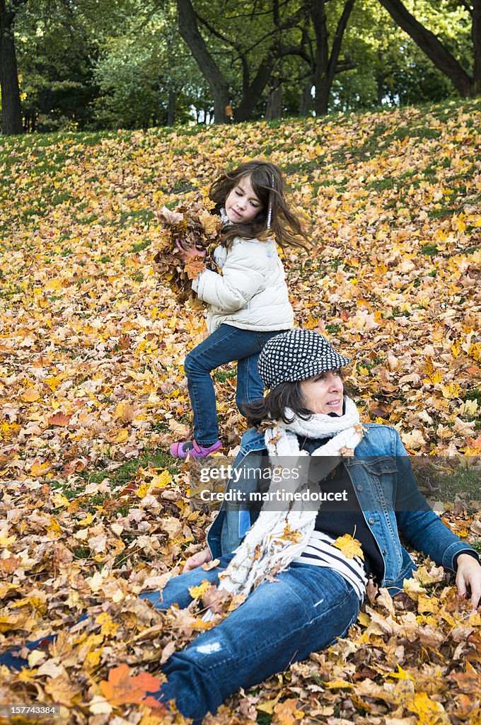 Mischievous daugther about to pitch autumn leaves on her mother.