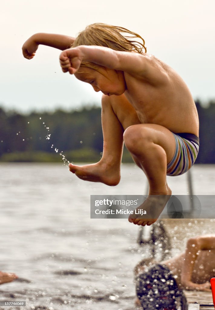 Boy jumps into water from a bathing platform