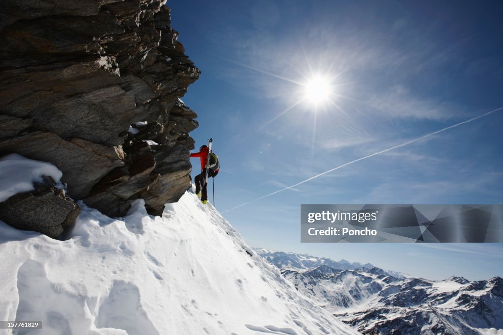 Man walking up a mountain with skis