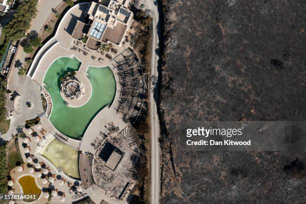 An area ravaged by wildfire stands next to a hotel on the coastline on July 29, 2023 in Lardos, Rhodes, Greece. While A firefighting helicopter is...