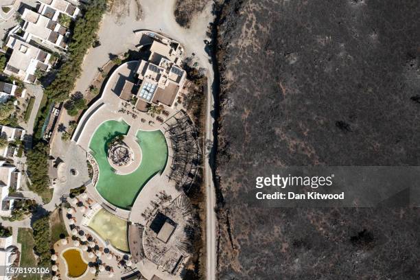 An area ravaged by wildfire stands next to a hotel on the coastline on July 29, 2023 in Lardos, Rhodes, Greece. While A firefighting helicopter is...