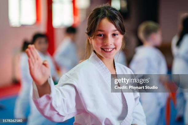 little girl training during a karate class, looking at camera and smiling - child judo stock pictures, royalty-free photos & images