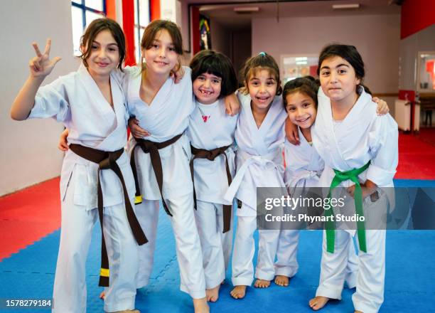 a group of elementary age children are taking a martial arts class. they are standing together in a row and are smiling while looking at the camera. - judo stockfoto's en -beelden