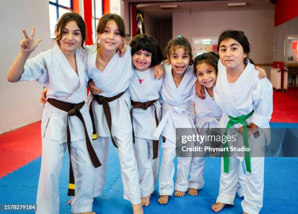 a group of elementary age children are taking a martial arts class. they are standing together in a row and are smiling while looking at the camera. - judo stock pictures, royalty-free photos & images