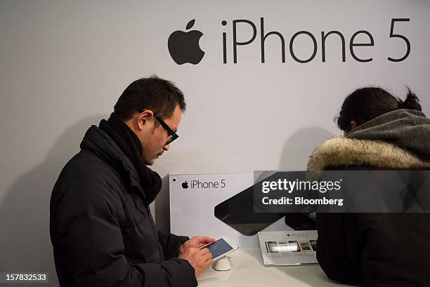 Customers examine an Apple Inc. IPad Mini, left, and iPhone 5 during a launch event organized by SK Telecom Co. In Seoul, South Korea, on Thursday,...