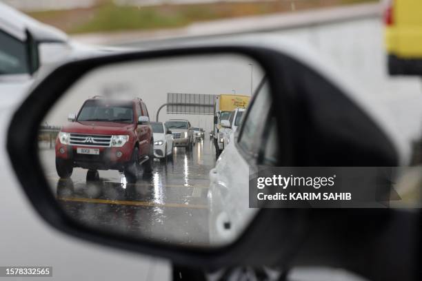 Motorists driving along a flooded street are photographed through a side view mirror of a vehicle, on a rainy day in Dubai on August 5, 2023.