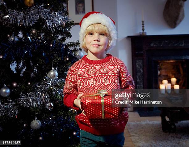 child holding christmas present beside tree. - christmas sweater stockfoto's en -beelden