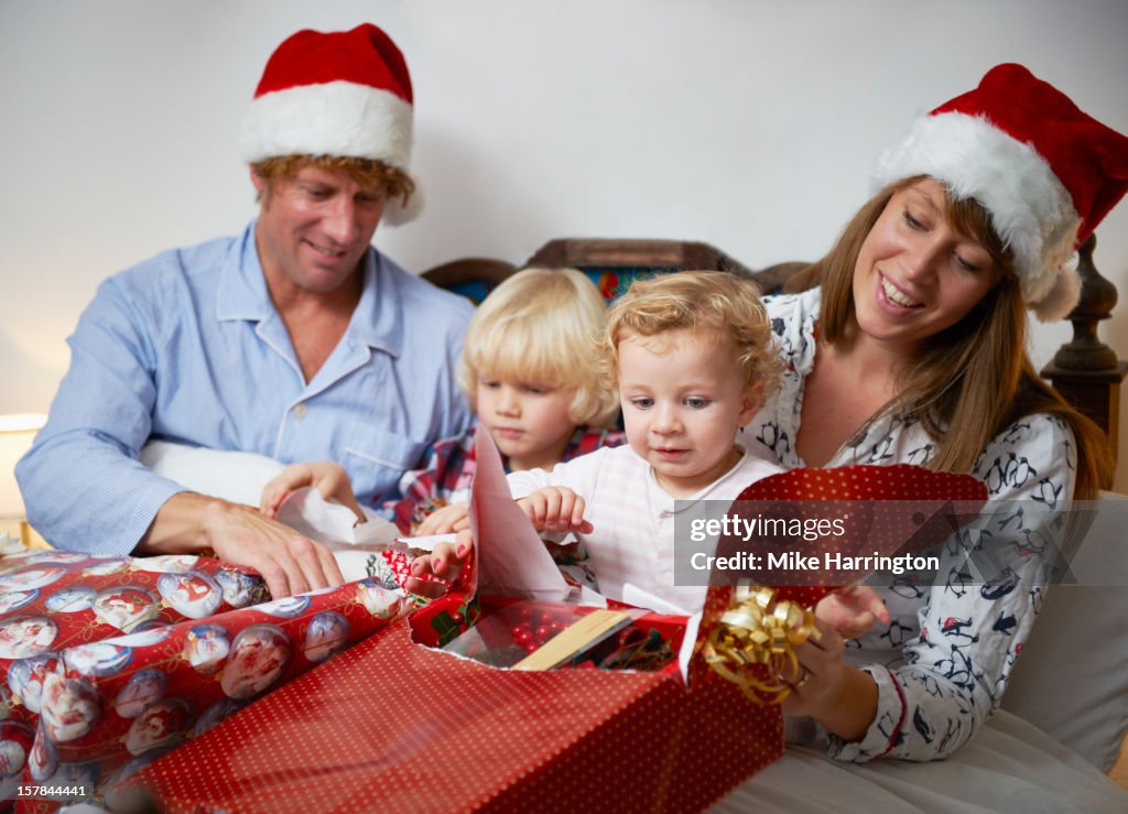 Family in bed at Christmas opening presents.