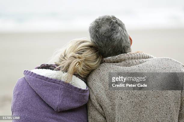couple sat on beach in winter looking out to sea - woman finding grey hair stock pictures, royalty-free photos & images