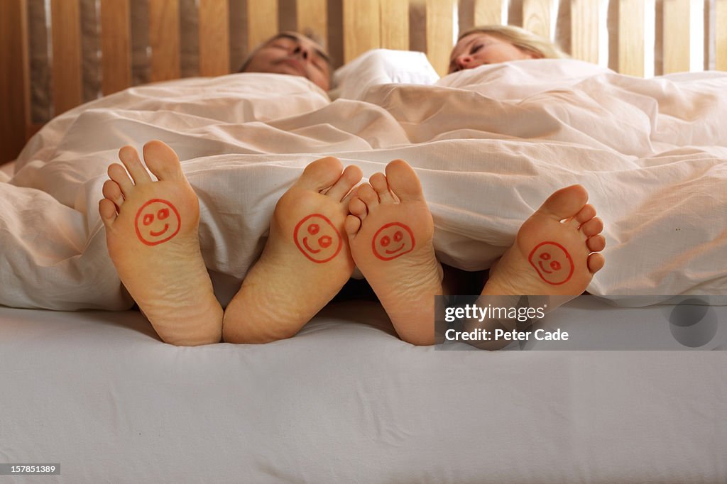 Couple in bed, happy faces drawn on feet