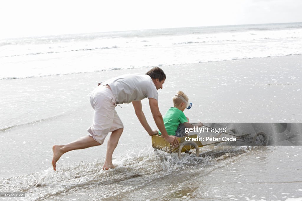 Father pushing son in go-kart on beach