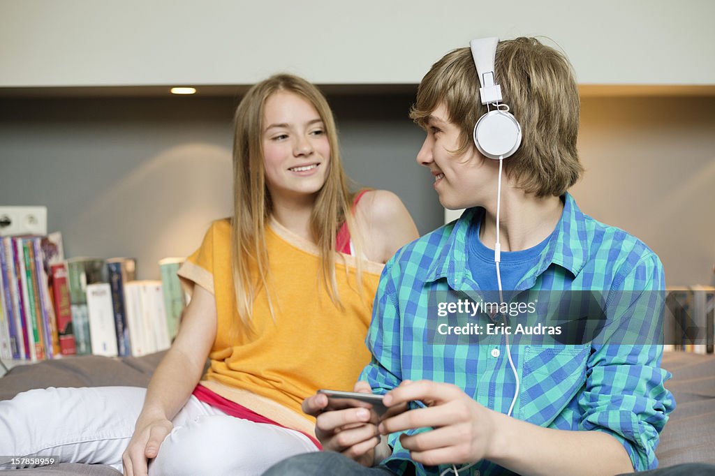 Teenage boy listening to music on iPod with his sister at home