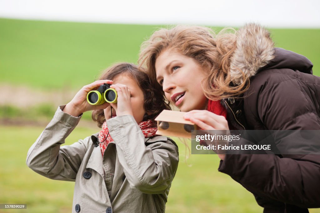 Boy looking through binoculars standing with his mother