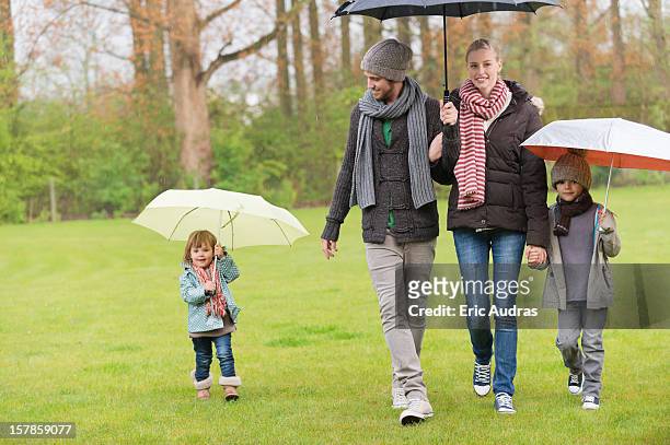 family walking with umbrellas in a park - mother protecting from rain stockfoto's en -beelden