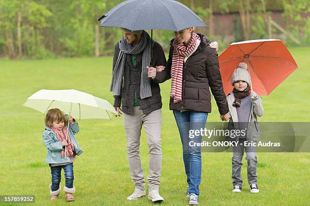 family with umbrellas in a park - mother protecting from rain stock-fotos und bilder