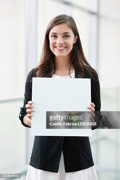 portrait of a businesswoman holding a blank placard and smiling in an office - placard stockfoto's en -beelden