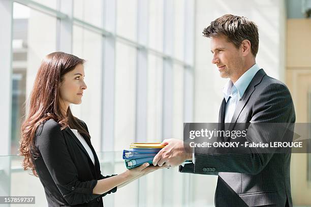 businessmen giving files to his female colleague in an office - adult man brussels stock pictures, royalty-free photos & images