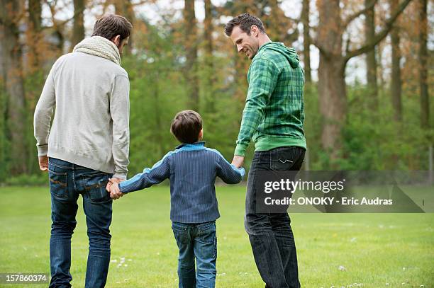 rear view of a boy walking with two men in a park - adoption stock pictures, royalty-free photos & images