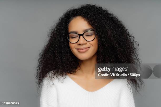 smiling woman,bushy hair,closed eyes,glasses,white jumper,imagines,dark grey wall - editorial template stock pictures, royalty-free photos & images