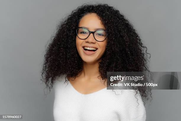 curly woman laughs,good mood,healthy skin,glasses,white sweater,grey background - editorial template stock pictures, royalty-free photos & images