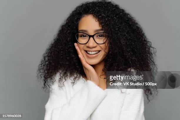 afro woman smiles,touch cheek,enjoys compliment,shy,white sweater,indoor pose - editorial template stock pictures, royalty-free photos & images