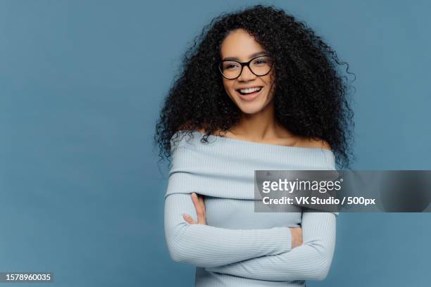 cheerful student,curly hair,arms folded,positive expression,blue sweater,indoors - editorial template stock pictures, royalty-free photos & images