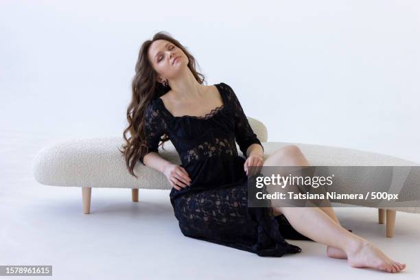 young attractive woman leans on beige sofa on white background - editorial template stock pictures, royalty-free photos & images