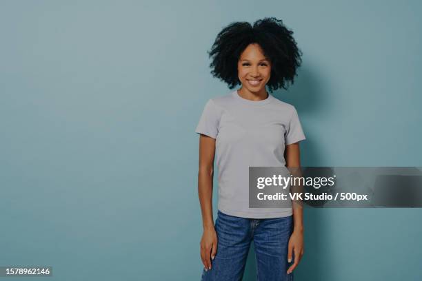 delighted young african female posing isolated over blue background with pleasant smile - editorial template stock pictures, royalty-free photos & images