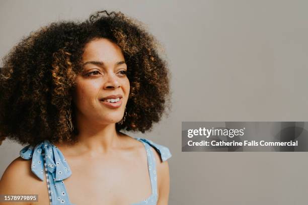 portrait of a young multiracial woman with natural curly hair against a plain backdrop - woman facial expression stock pictures, royalty-free photos & images