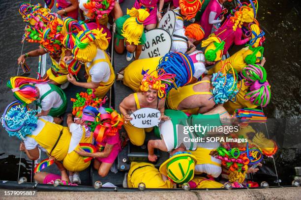 People wearing colorful clothes and wigs are seen going down under a bridge during the event. The Canal Parade starts around noon and takes all...