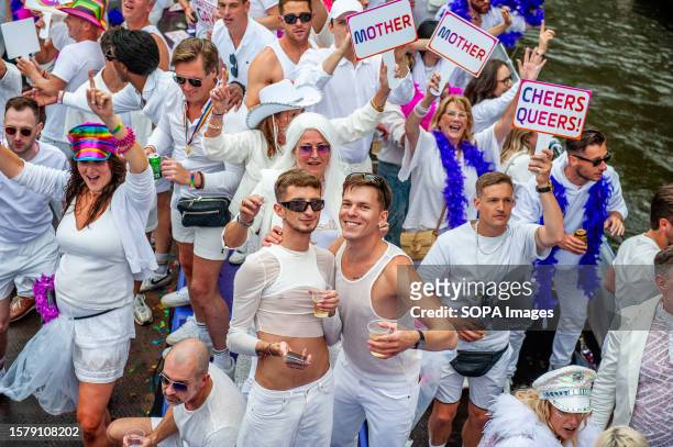 Gay couple wearing white clothes is seen looking at the camera during the event. The Canal Parade starts around noon and takes all afternoon. Around...