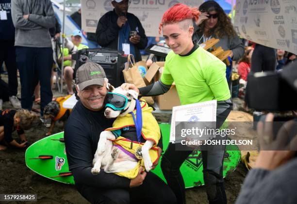 Faith and owners Mike Wall and James Wall celebrate after winning the large dog category of the World Dog Surfing Championships in Pacifica,...