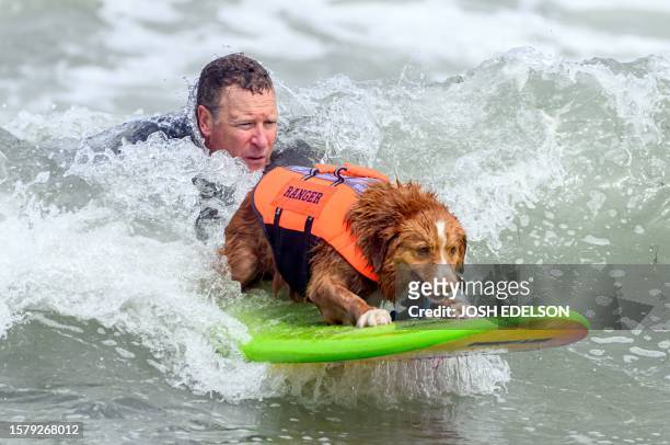 John Hill helps his dog Ranger catch a wave during the World Dog Surfing Championships in Pacifica, California, on August 5, 2023. The event helps...