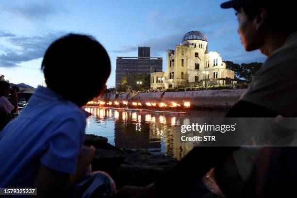 People watch as lanterns are lit and placed on the Motoyasu river by the Atomic Bomb Dome in remembrance of the victims in Hiroshima on August 5 on...