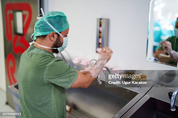 surgeon wearing scrubs washing hands before operation - schoonschrobben stockfoto's en -beelden
