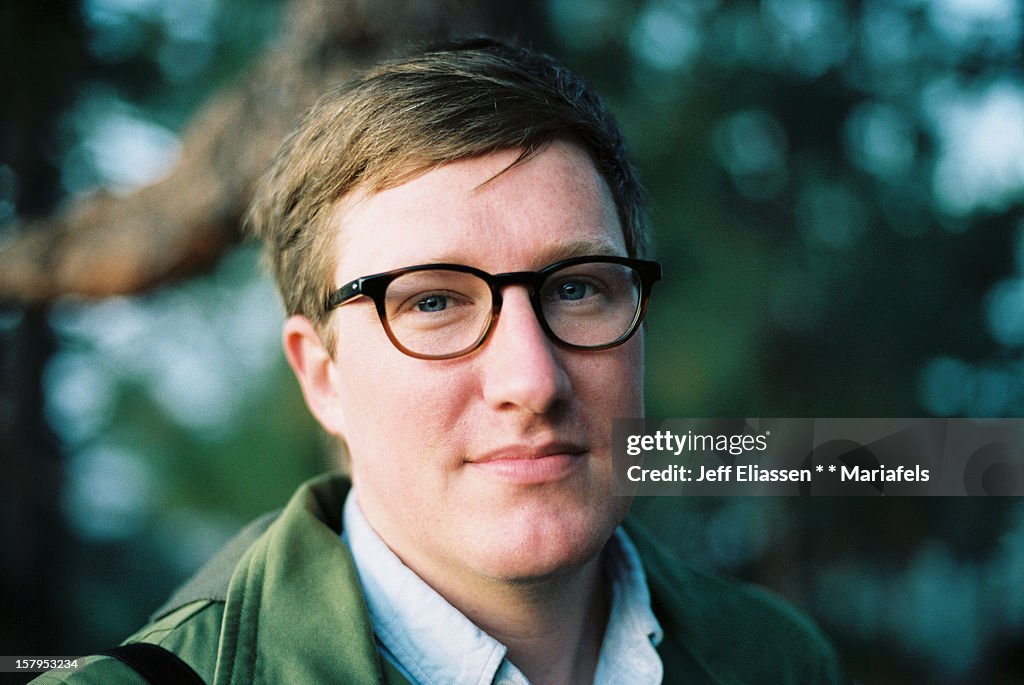 Male with glasses smiles at sunrise, trees behind