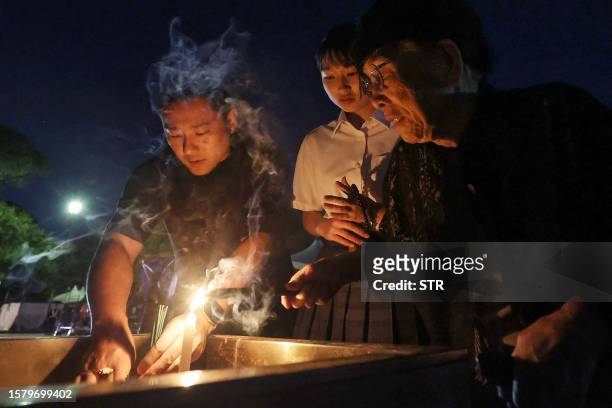 Visitors burn incense to remember the victims as they visit the cenotaph for the atomic bomb victims before sunrise at the Peace Memorial Park in...
