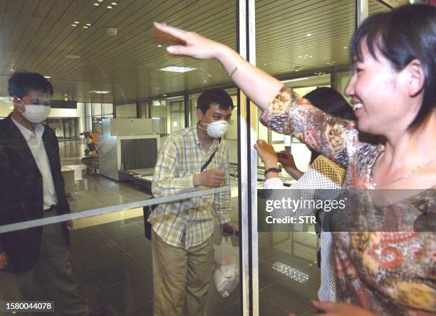 Relatives wave to Vietnamese students returning from China through a glass wall at Hanoi airport on 02 May 2003. Vietnam's health ministry said...