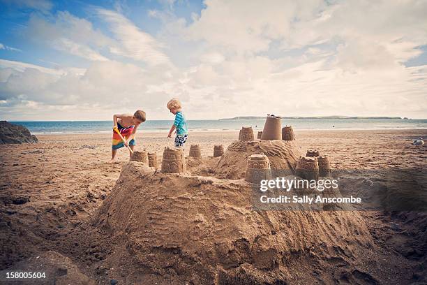 two little boys building sandcastle on beach - zandkasteel stockfoto's en -beelden