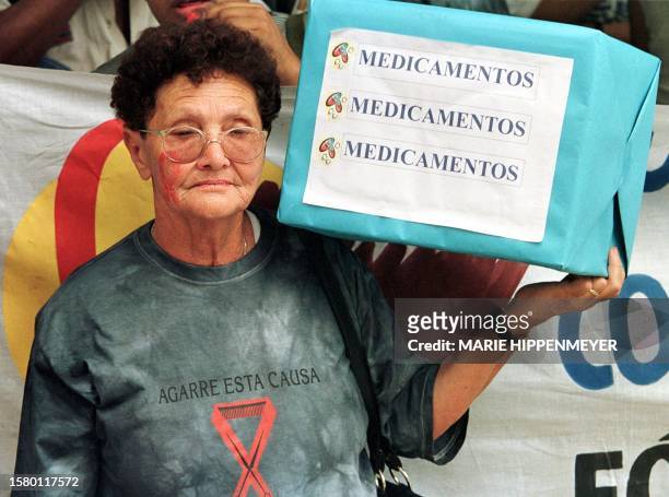 Demonstrator joins a protest against the lack of AIDS medicines. Una mujer carga una caja ficticia de medicamentos durante una protesta por la...