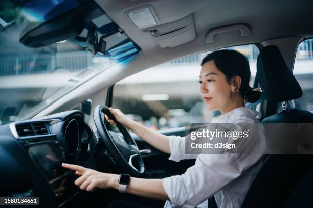 young asian woman sitting in car and touching screen, setting up gps navigation system for her destination. on the move. car rental. transportation with technology concept - car insurance stock pictures, royalty-free photos & images