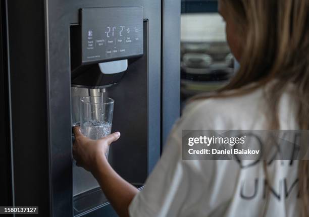 girl filling up glass of cold water from fridge. - girl filling water glass stock pictures, royalty-free photos & images