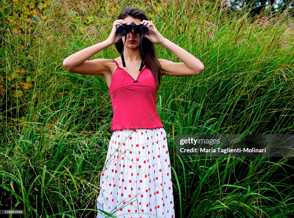 Young woman in tall green grass with binoculars