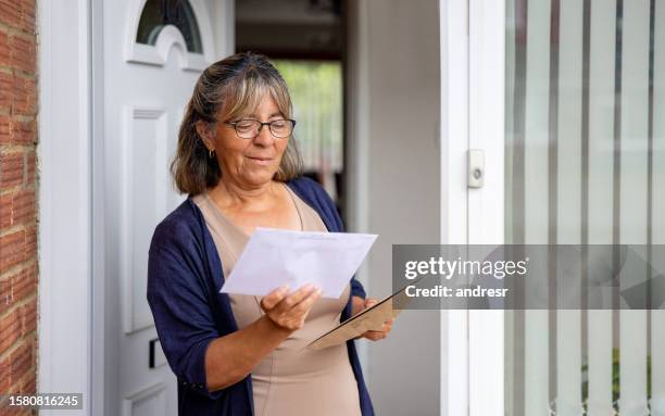 mature woman at the front door of her house checking her mail - woman opening door stock pictures, royalty-free photos & images